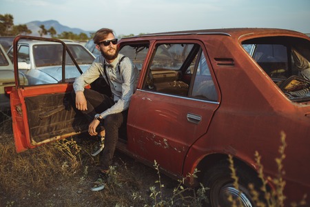 Portrait of a young handsome stylish man, wearing shirt and bow-tie with old carsの写真素材