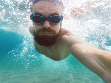 Young bearded man diving in a blue clean waterの写真素材