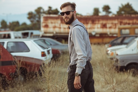 Portrait of a young handsome stylish man, wearing shirt and bow-tie on the field of old carsの写真素材