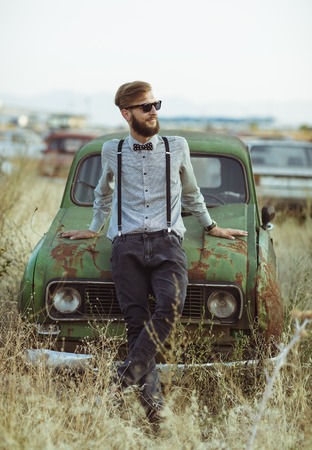 Portrait of a young handsome stylish man, wearing shirt and bow-tie with old carsの写真素材
