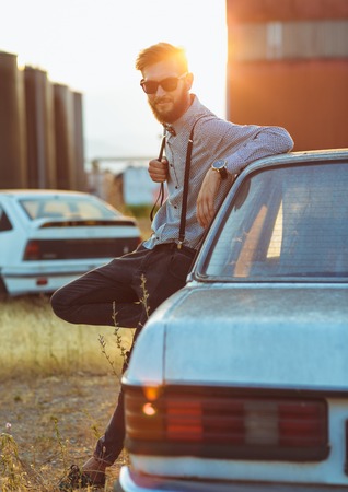 Portrait of a young handsome stylish man, wearing shirt and bow-tie with old carsの写真素材