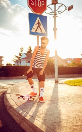 Young stylish man in sunglasses with a skateboard on a street in the city at sunset lightの写真素材