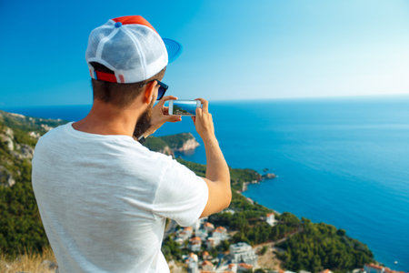 Man makes photos by a smartphone on the background of sea coast, Adriatic sea, Montenegro, Balkansの写真素材