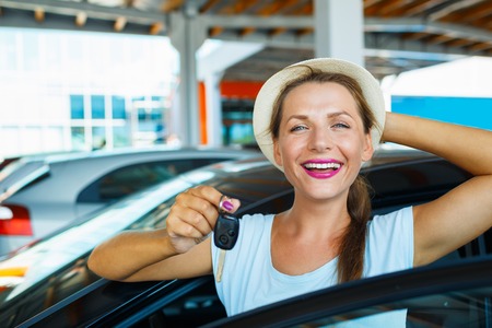 Young happy woman standing near a car with keys in hand - concept of buying a used carの写真素材