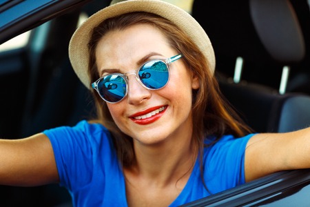 Young smiling woman in hat and sunglasses making self portrait sitting in the carの写真素材
