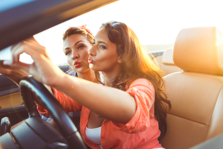 Two young beautiful girls are doing a photo of yourself in a convertibleの写真素材