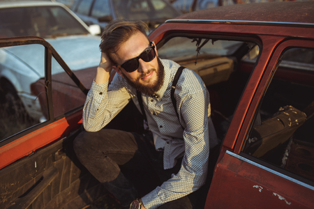Portrait of a young handsome stylish man, wearing shirt and bow-tie with old carsの写真素材