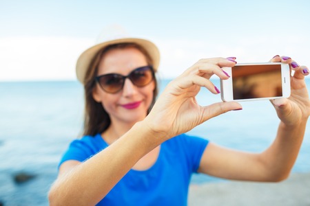 Girl in the hat making selfie by the smartphone on the background of sea coast, Adriatic sea, Montenegro, Balkansの写真素材