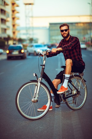 Young stylish man in sunglasses riding a bike on city streetの写真素材