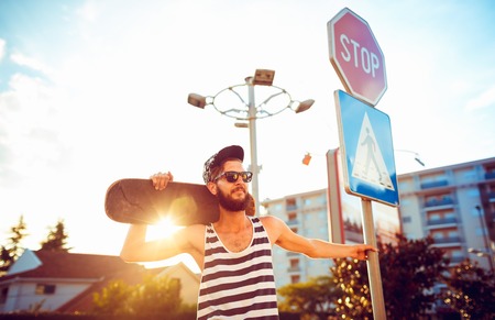 Young stylish man in sunglasses with a skateboard on a street in the city at sunset lightの写真素材
