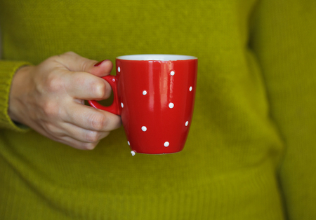 Woman hand holding a cozy red mug.の写真素材