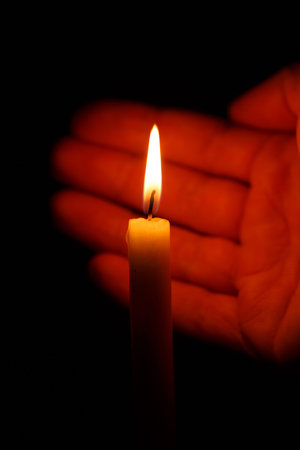 Hand protects the flame of a burning candle on a black background