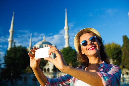 Girl in the hat making selfie by the smartphone on the background of the Blue Mosque, Istanbul. Turkeyの写真素材