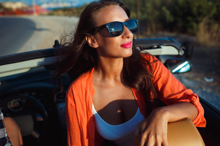 Beautiful woman sitting in cabriolet, enjoying trip on luxury modern car with open roof, fashionable...