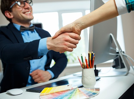Young businessman and businesswoman shaking hands in officeの写真素材