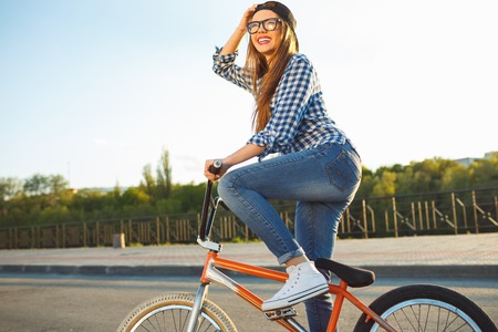 Lovely young woman in a hat riding a bicycle on city background in the sunlight outdoor. Active peopleの写真素材