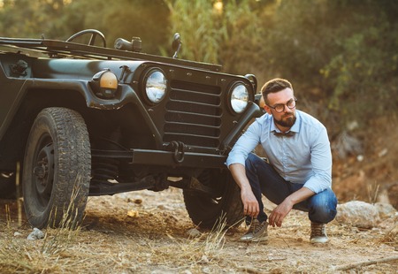 Young stylish man with glasses and bow tie near the old-fashioned SUV on the sunsetの写真素材