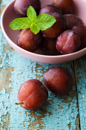 Bowl with plums on blue shabby wooden background. Agriculture, gardening, harvest concept.の写真素材