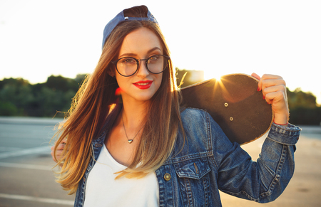 Fashion lifestyle, Beautiful young woman with skateboard, backlit at sunsetの写真素材