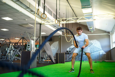 Athletic man with battle rope in functional training fitness gym