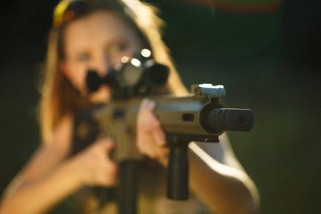 A young girl with a gun for trap shooting aiming at a target. Short depth of field, focus on the...