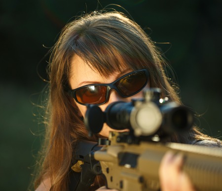 A young girl with a gun for trap shooting and shooting glasses aiming at a targetの写真素材