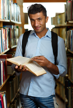 Young arab student reading book between the shelves in the libraryの写真素材