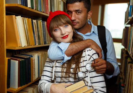 Young student couple choosing books between the shelves in the library