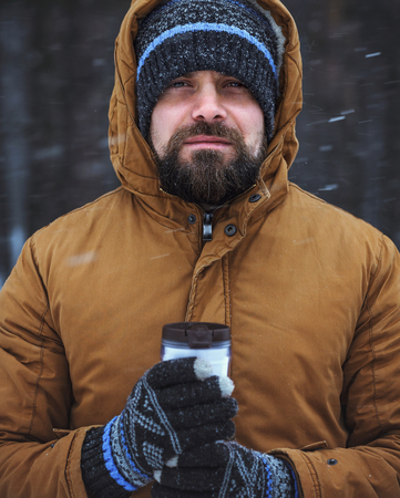 Beard man with hot drink in thermos cup in cold winter forestの写真素材
