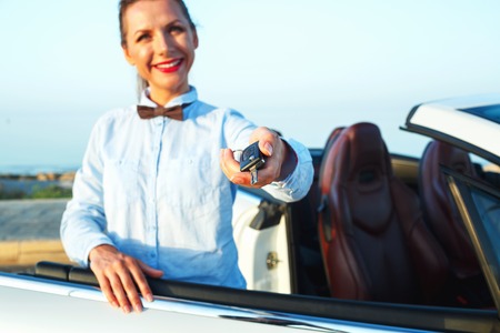 Young woman standing near a convertible with keys in hand - concept of buying a used car or a rental carの写真素材