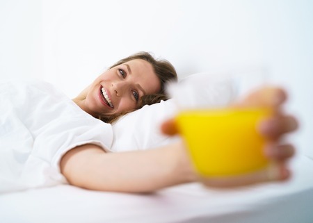 Cute woman sleeping in bed waking up stretching, smiling and drinks orange juice in bed in the morningの写真素材