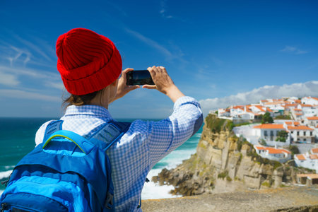 Woman in red hat with a backpack makes a photo on the smartphone of a beautiful panorama of the...