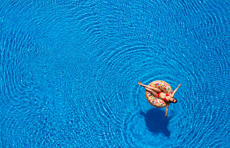 Aerial view of a woman in red bikini lying on a donut in the pool. Concept of summer rest and...