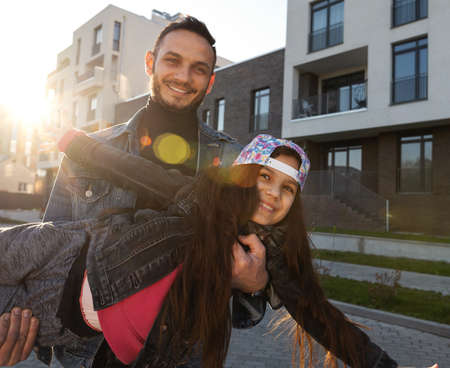 Father holding his daughter in his arms near the house at sunset, happy family day.の写真素材