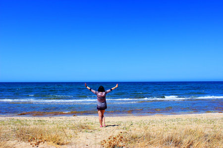 A girl stands on the beach and pulls hands to the sky on a sunny dayの写真素材