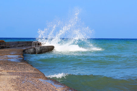 Sea water storm waves hitting the stone pier, sunny and windy dayの写真素材
