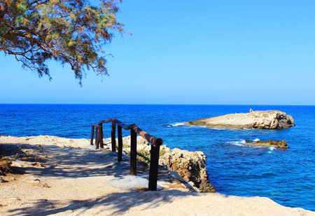 View of the sea and the island from the cliffs on the edge of which are railing, in the shade of a tree for rest and relaxationの写真素材