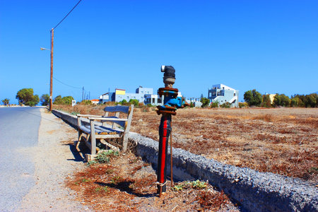An old Fire Hydrant stands next to a bench in the middle of a street on the coast in sunny weather with blue skies and heatの写真素材