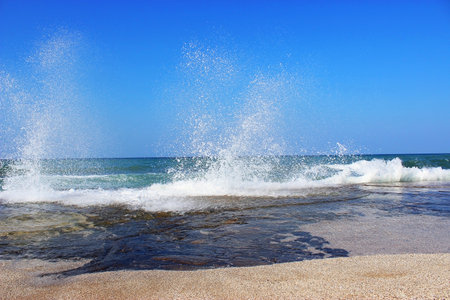 Sea water storm waves hitting the big stone on the beach on a sunny and windy dayの写真素材