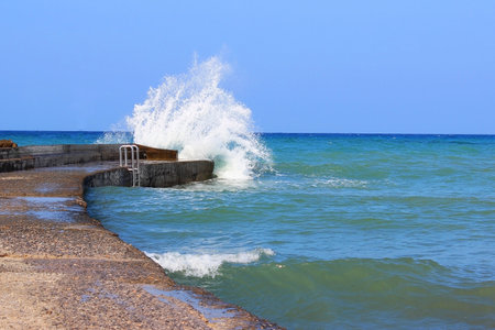 Sea water storm waves hitting the stone pier, sunny and windy dayの写真素材