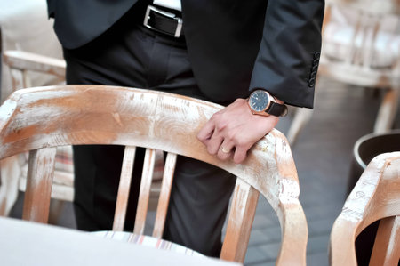 Black suit groom with hand and wristwatch on restaurant chairの写真素材