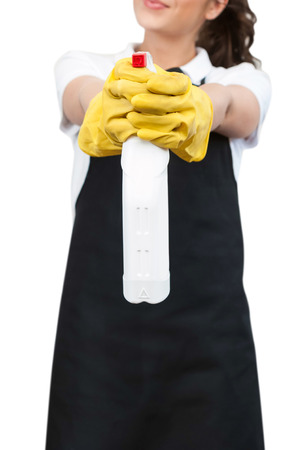 Closeup of a Spring cleaning Woman with black apron and yellow gloves, pointing a spray bottle at the camera on a white backgroundの写真素材