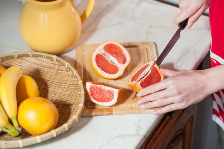 Female hands cutting fresh juicy grapefruit on wooden boardの写真素材
