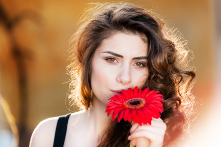 Young woman outdoors portrait. Soft sunny colors on a summer sunny day holding a red flower.の写真素材