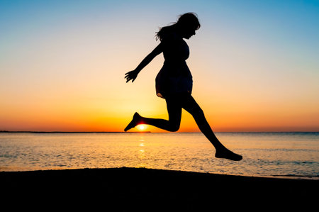 Silhouette of woman jumping in the air on the beach at sunrise.の写真素材