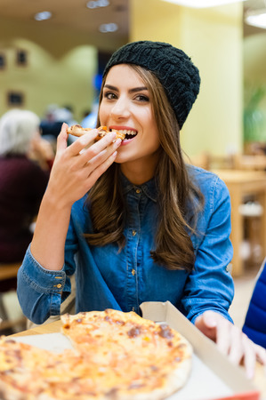 A young woman sitting in a restaurant, smiling,looking at the camera holding a slice of pizza.の写真素材