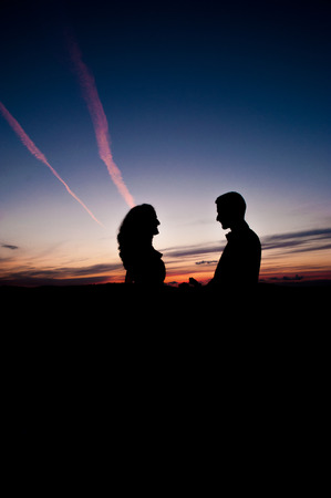 Silhouette of Young couple in love bride and groom posing in a field on beautiful sky sunset background, in their wedding day in the summer,holding hands. Series.の写真素材