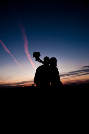 Silhouette of Young couple in love bride and groom posing in a field on beautiful sky sunset background, in their wedding day in the summer. Seriesの写真素材