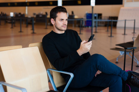 Portrait of handsome smiling man in casual wear, with his mobile phone while sitting in the hall of...