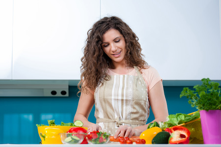Young woman cooking in the kitchen healthy food, vegetable Salad. Holding a knife and cutting vegetables on a cutting board.の写真素材